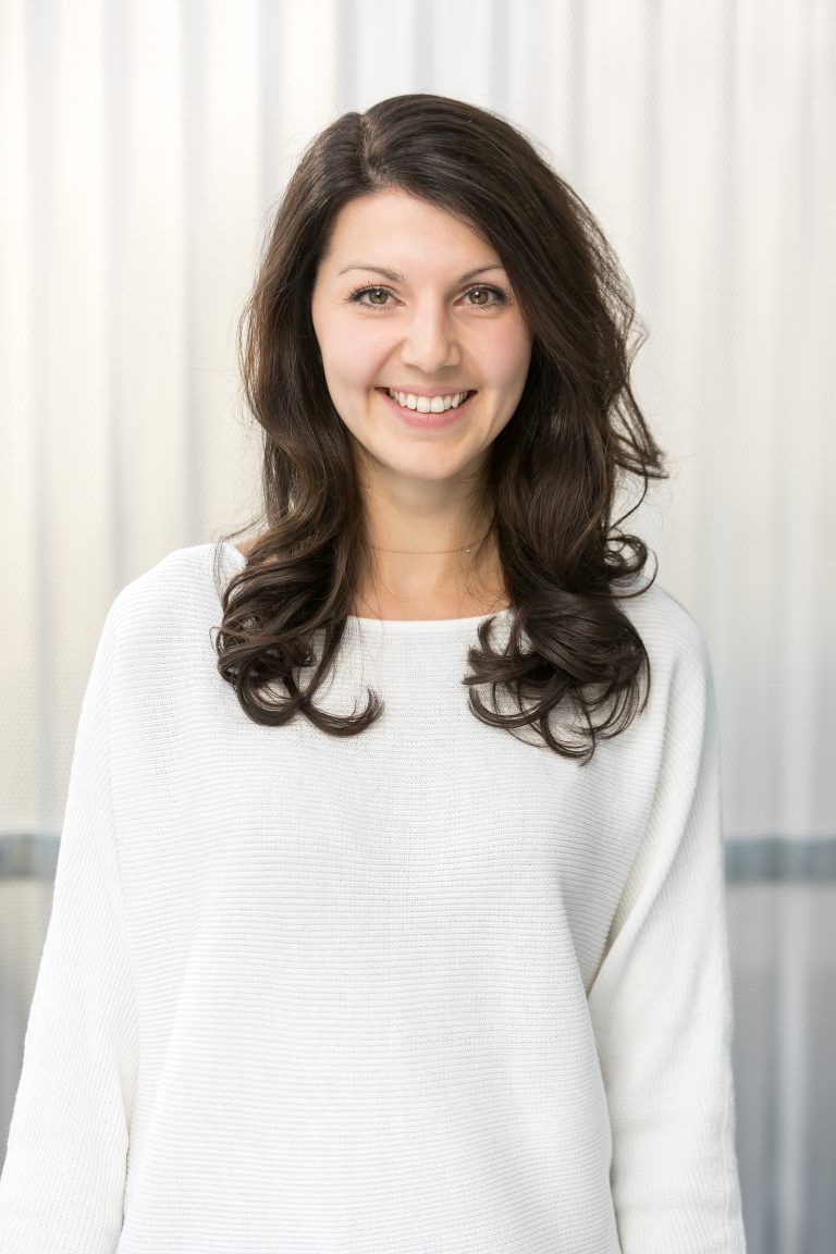 Frau mit dunklen Haaren und weißem Pullover im Portrait.